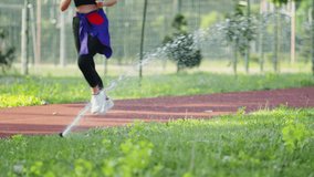 Automatic rotating irrigation sprinkler watering green lawn in public park. Unrecognizable woman engages in a healthy lifestyle by jogging on a red running track - Powered by Shutterstock - Get 15% off with code: PIKWIZARD15