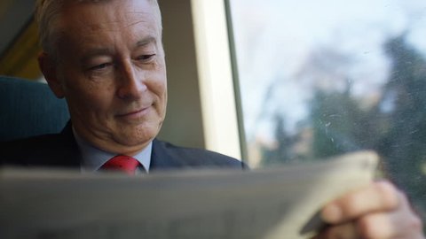 Business man on a train checking share prices in a paper, in slow motion