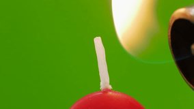 Light a candle on a green background, chroma key. Light a red candle with a lighter, close-up macro. Congratulations on the holiday birthday