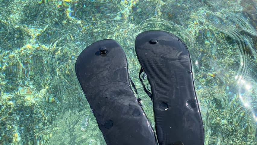 Floating black upside down flip flops in transparent turquoise sea water by the beach in Spain, fun sunny summer vacation holiday shoes, 4K shot Royalty-Free Stock Footage #3413006357