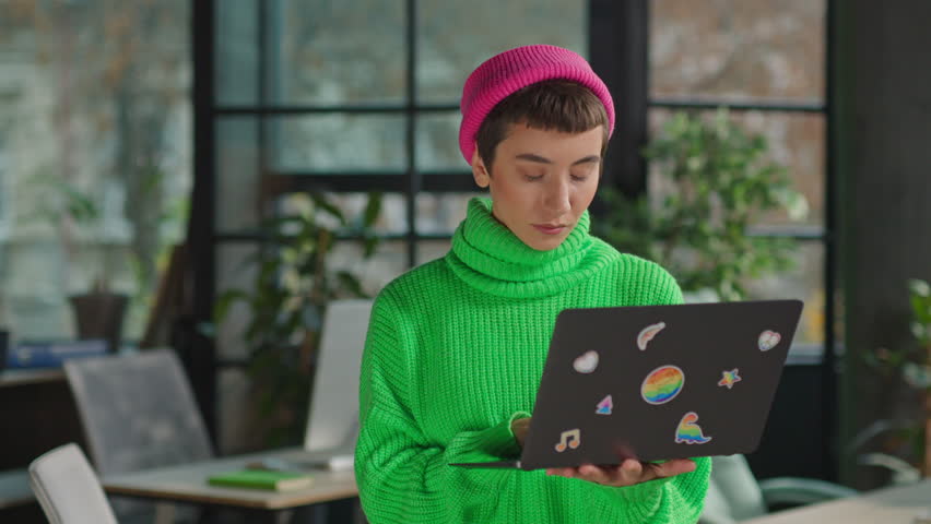 Smiling young gay woman holding laptop with rainbow stickers looking at camera