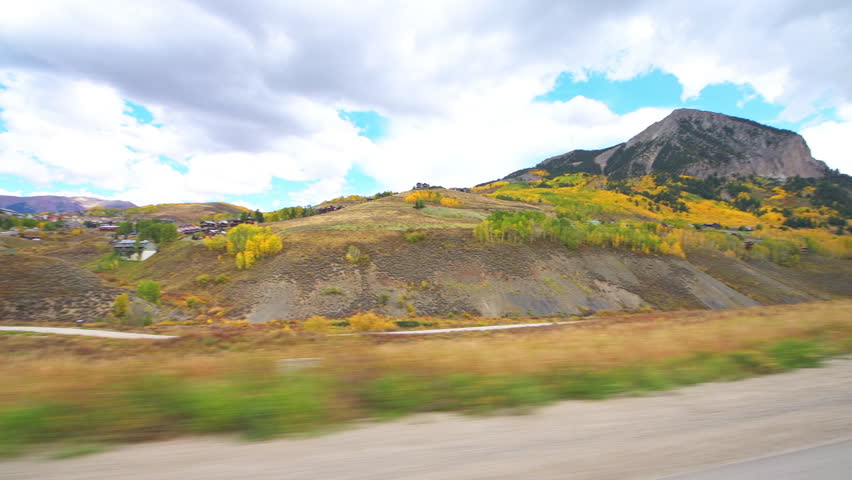Mount Crested Butte, Colorado village town car vehicle driving shot side view in autumn at Rocky mountains by buildings houses