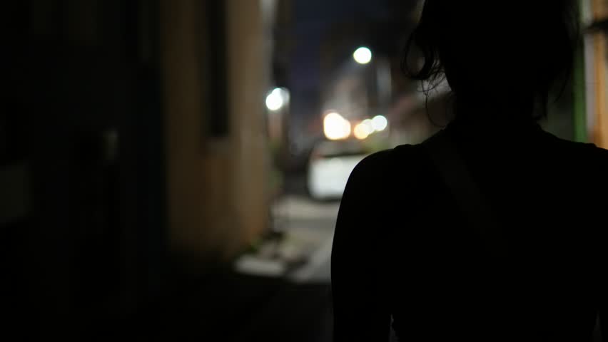 Unrecognizable young girl with solitude walking alone on a dimly lit street at night.