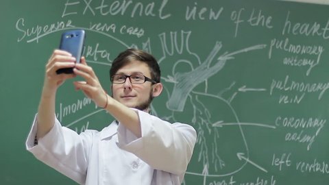 young student photographing himself against a blackboard background