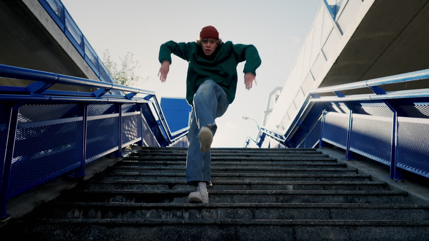 Fashion modern man in beanie hat dancing outside at the city stairs