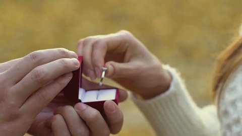 Woman putting on diamond ring on finger in park, luxury expensive jewelry