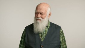 Elderly man with a long white beard and cheerful expression wearing a black vest over a plaid shirt, standing against a neutral background, exuding warmth, wisdom, and a sense of calm. Camera 8K RAW. - Powered by Shutterstock - Get 15% off with code: PIKWIZARD15