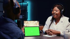 Woman invited to podcast watching internet clips on green screen tablet with host in studio, discussing content. African american guest reacting to videos on mockup device during online comedy show