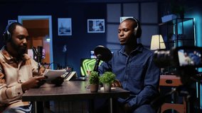 African american host engaging in entertaining discussion with man during livestream in apartment studio, making him laugh. Presenter uses high tech filming gear to produce comedy podcast