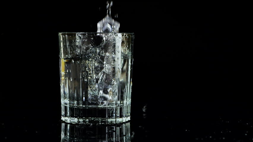 Ice cubes falling into a glass of water on a black background. Slow motion. Isolated on black background.