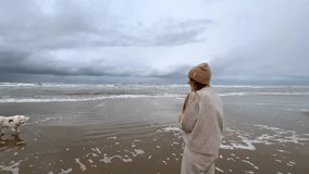 a girl in woolen clothes walks along a wide beach near the northern sea. enjoying nature, listening to the sound of the sea, the north wind blowing on her develops her hair. High quality video