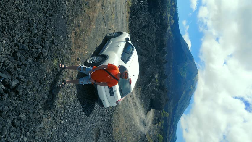 A man stands by a car in the middle of a frozen black lava field on a volcano. Aerial drone view.