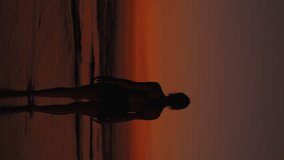 Vertical video. Charming Sporty Woman on Seashore Gracefully Performs Exercise During Her Fitness Routine. Athlete Showing Her Flexibility by Stretching Hands Against Backdrop of Beautiful Sunset