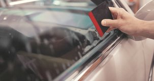 Car tinting windows - Worker specialist apply tint foil on car window in workshop video 4K