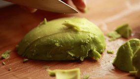 cutting avocado into cubes on wooden board close up