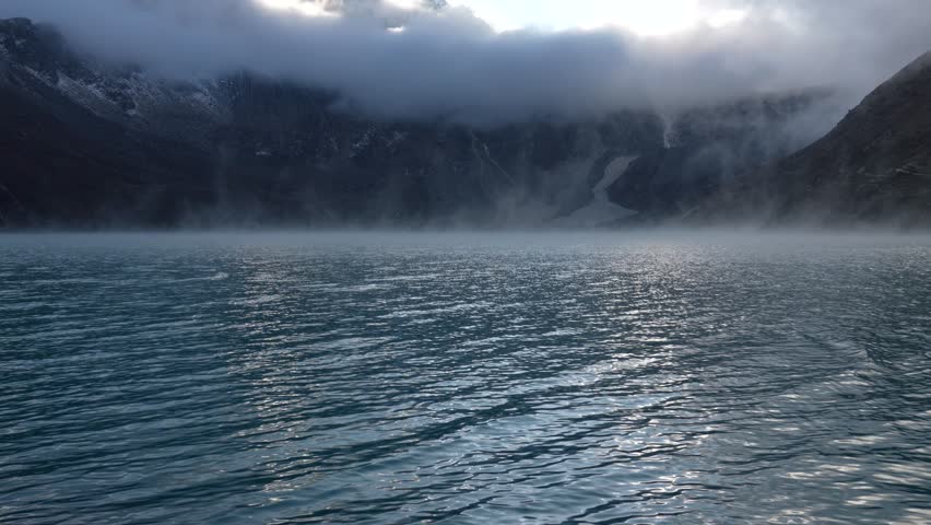 Fog creeps over the surface of the water in a lake in the Himalayan mountains