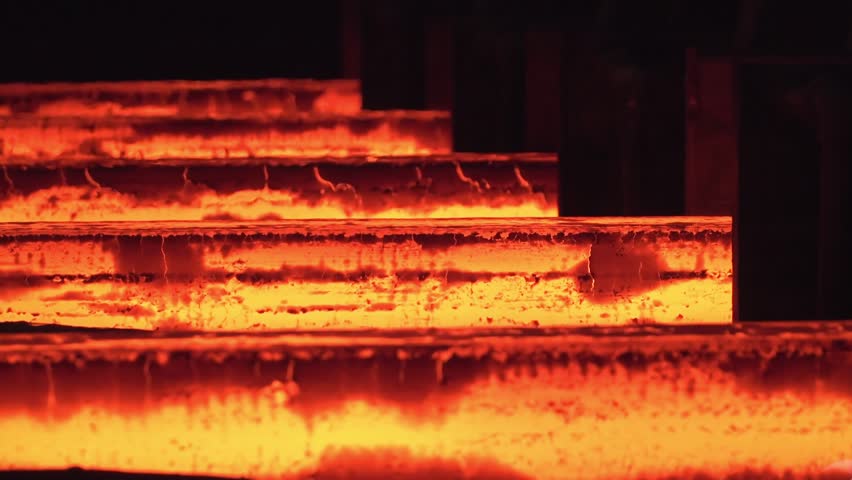 Metallurgy factory. Steel production in the workshop. Hot metal sheet slides along the conveyor. Heavy industry. Red hot steel metal billets after molten steel casting. Hot steel bars on the conveyor.