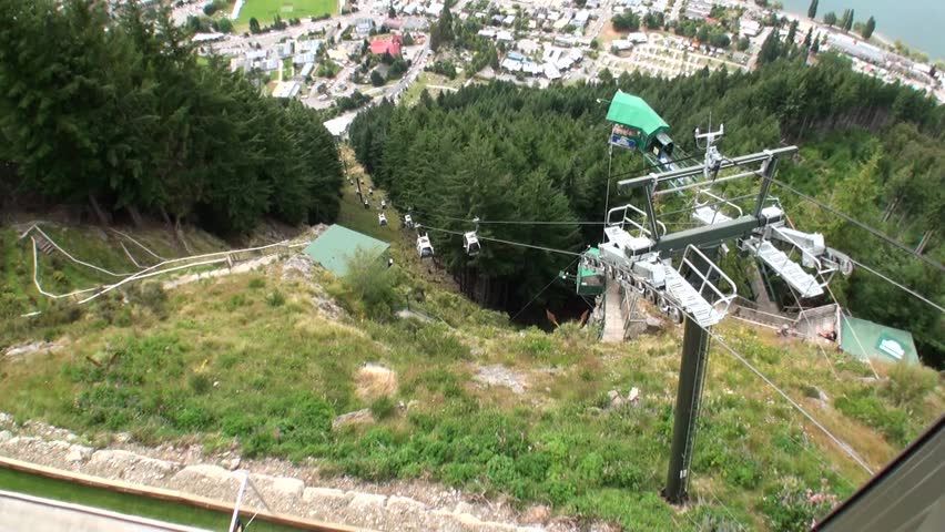 Aerial cableway lift in mountains of New Zealand. People in cabins or chairs suspended from rope.