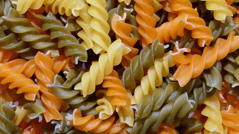 Multicolored Pasta rotating in slow motion top view. Rotation of Colored spiral pasta 4k. heap of Uncooked pasta. Italian food close up. Delicious italian fusilli.  tricolor pasta. food background