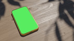 A phone lying on a table, an animation of a gadget on a wooden table. the video has a green screen with shadows from the foliage