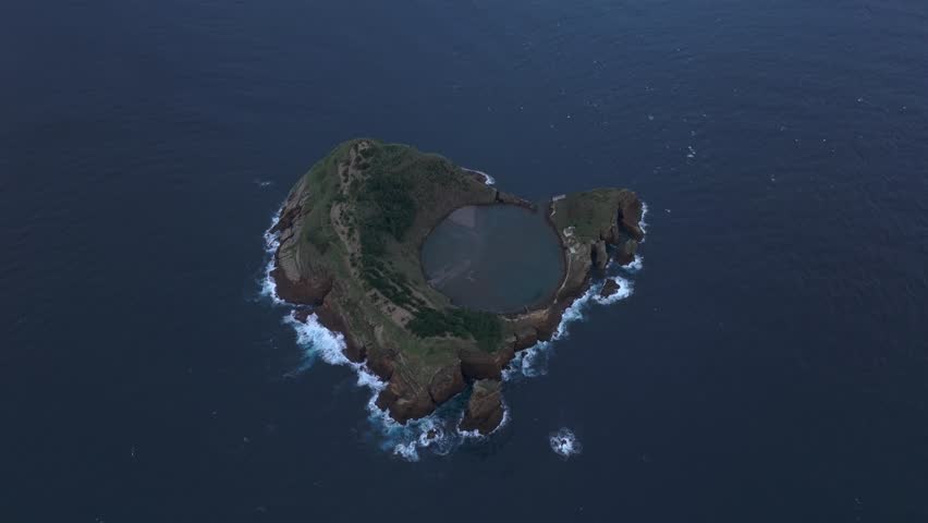 Reveal shot of Ilhéu de Vila Franca do Campo with Vila Franca do Campo city in background, aerial