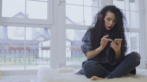 Charming brunette with red lips listen music with headphones and use phone