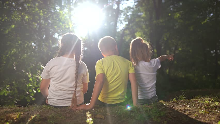 children sit on the banks of river. happy family childhood dream concept. a group of little children sit together by the river and lifestyle talk. kids spend time outdoors in nature in the forest
