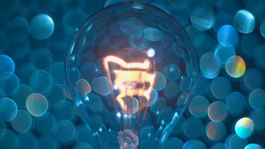 An old high-wattage and not economical incandescent lamp with a tungsten filament shines with a pleasant warm light against the backdrop of beautiful shiny colorful bubbles bokeh. Closeup. Macro Royalty-Free Stock Footage #3414027399