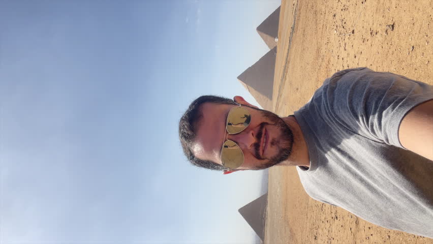 Tourist man makes victory sign with the pyramids of Giza in the background, Egypt. Achievement, satisfaction. Vertical