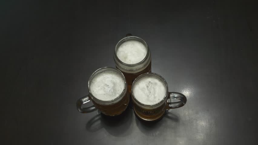 Three men drinking lager near the bar counter. Close up of male hands clinking their glasses top view. Caucasian guys raising their beer mugs at the pub