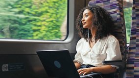 Young businesswoman commuting sitting on moving train passing through city working on laptop and listening to music or podcast on earphones looking out of window - shot in slow motion - Powered by Shutterstock - Get 15% off with code: PIKWIZARD15