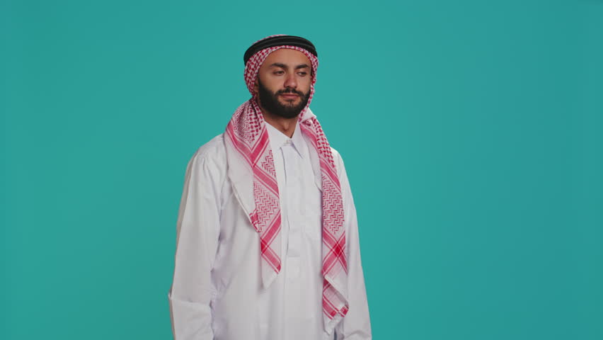 Middle eastern man having migraine over blue studio background, dealing with painful headache and pressure. Adult with traditional islamic clothing feeling hurt and worried, being stressed.