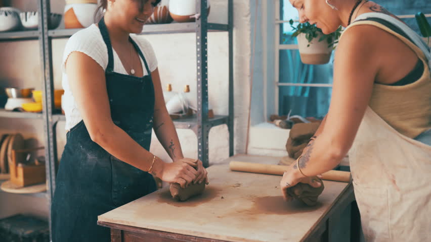 Woman, hands and kneading clay for pottery, small business or molding art together at workshop. Female person and colleague in store for creation, creativity or startup on table with ceramics indoors Royalty-Free Stock Footage #3414177931