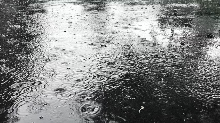 Close-up view of heavy rain falling into puddles on asphalt. Raindrops on the road for the background. Asphalt is wet due to puddles of rainwater.