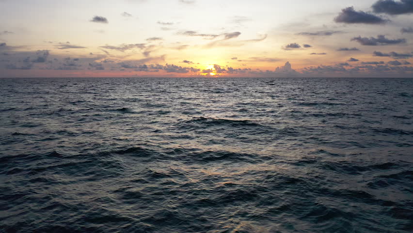Flying over the ocean waves during sunset as the sun disappears into night. bird eye view 4K cinematic drone footage.