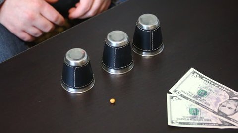 Thimblerig. A man hides a pea under one of the glasses, moves them on the table. The player points to the glass, but does not guess, and gives the win to the presenter. Cups and balls trick.