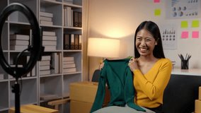 Blogger, vlogger small SME. Beautiful Asian woman uses mobile video calls to sell clothes. Live online sales, product details display at home office Ecommerce Entrepreneur Concept.