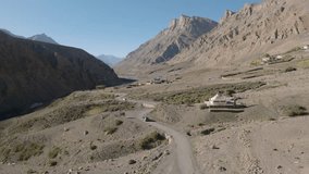 Aerial video by a drone in cold desert mountains of spiti valley following a black SUV car on the adventurous road through the mountains. Hiqh quality 4K video taken by a drone on a sunny day.