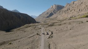 Aerial video by a drone following a black 4x4 car on country road through a cold desert landscape in the high altitude mountains on the way to Leh Ladakh.