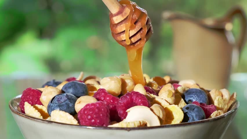Honey pouring from honey dipper in bowl with Oatmeal porridge. Adding natural honey to granola with fresh berries. Healthy organic honey dripping from the wooden spoon closeup. Healthy breakfast