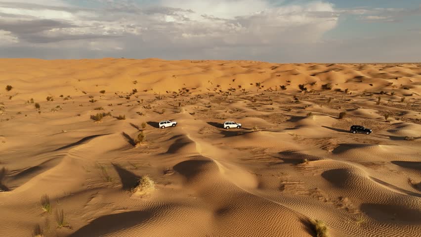 The drone is flying sideways following three cars driving through the Sahara desert in Tunisia Aerial Footage 4K