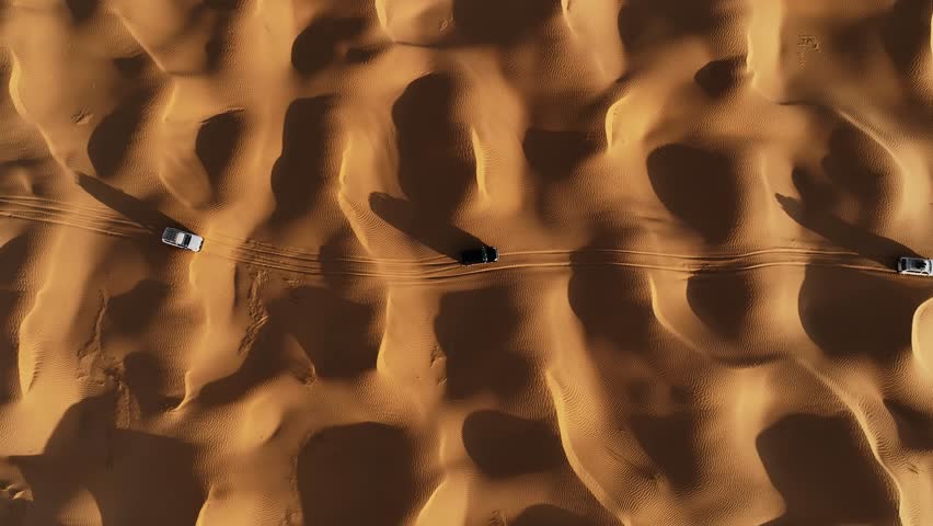 The drone is flying up looking topdown at three cars driving through the Sahara desert in Tunisia Aerial Footage 4K