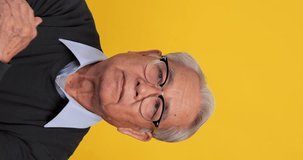Vertical clip. An old Asian man is thinking and deciding something. Isolated on yellow background in the studio.