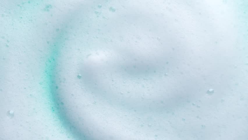 Foam texture backdrop on blue background. Liquid soap bubbles, Froth bubbles backdrop. Soap foam popping bubble rotating. Soap sud macro structure close-up. Clean, cleaning, washing, laundry. 
