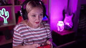 Blonde woman gaming with headphones in a neon-lit room at night, exhibiting excitement and focus.