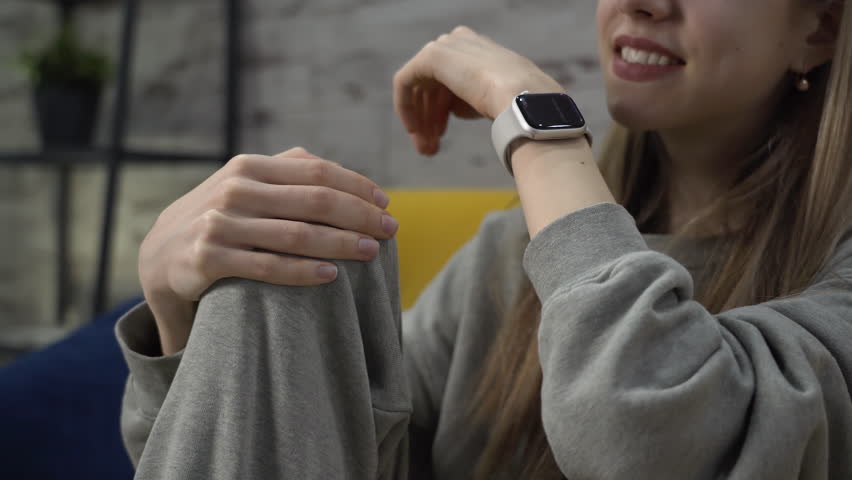 Woman sitting on sofa in living room and answering call on her smartwatch