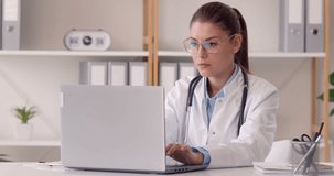 Friendly woman online doctor telehealth worker in glasses waves hello at office notebook PC, listens to patient, answers questions, gives medical advice, smiles and says goodbye at end of consultation