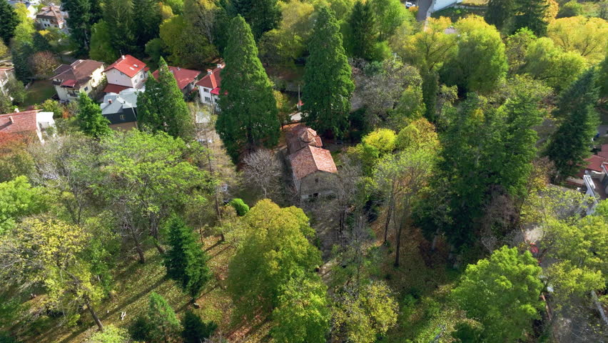 Flying around medieval Boyana church in Sofia, Bulgaria. Sturdy Orthodox Church from the times of Bulgarian Empire. Tall trees surround the church. The shot was made in mid Autumn. 
