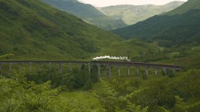 Picturesque stone viaduct over green valley crossed by a Jacobite steam train. Old locomotive on a railway journey through idyllic landscape of the Scottish Highlands with green valleys and mountains. - Powered by Shutterstock - Get 15% off with code: PIKWIZARD15