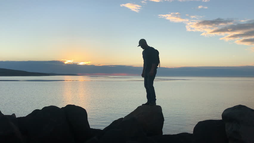 Ocean, rock and man hiking at sunset outdoor in nature, freedom and travel. Sea, adventure and person trekking in environment on summer holiday, vacation or walking by water for coastal journey view